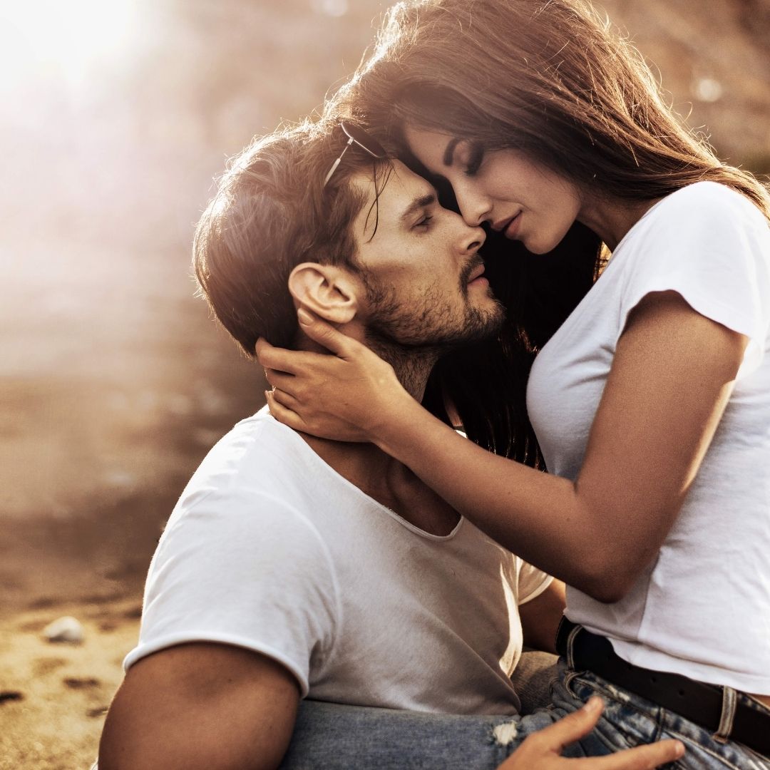 Image of a woman sitting on a mans lap with their faces close together just moments before a kiss.